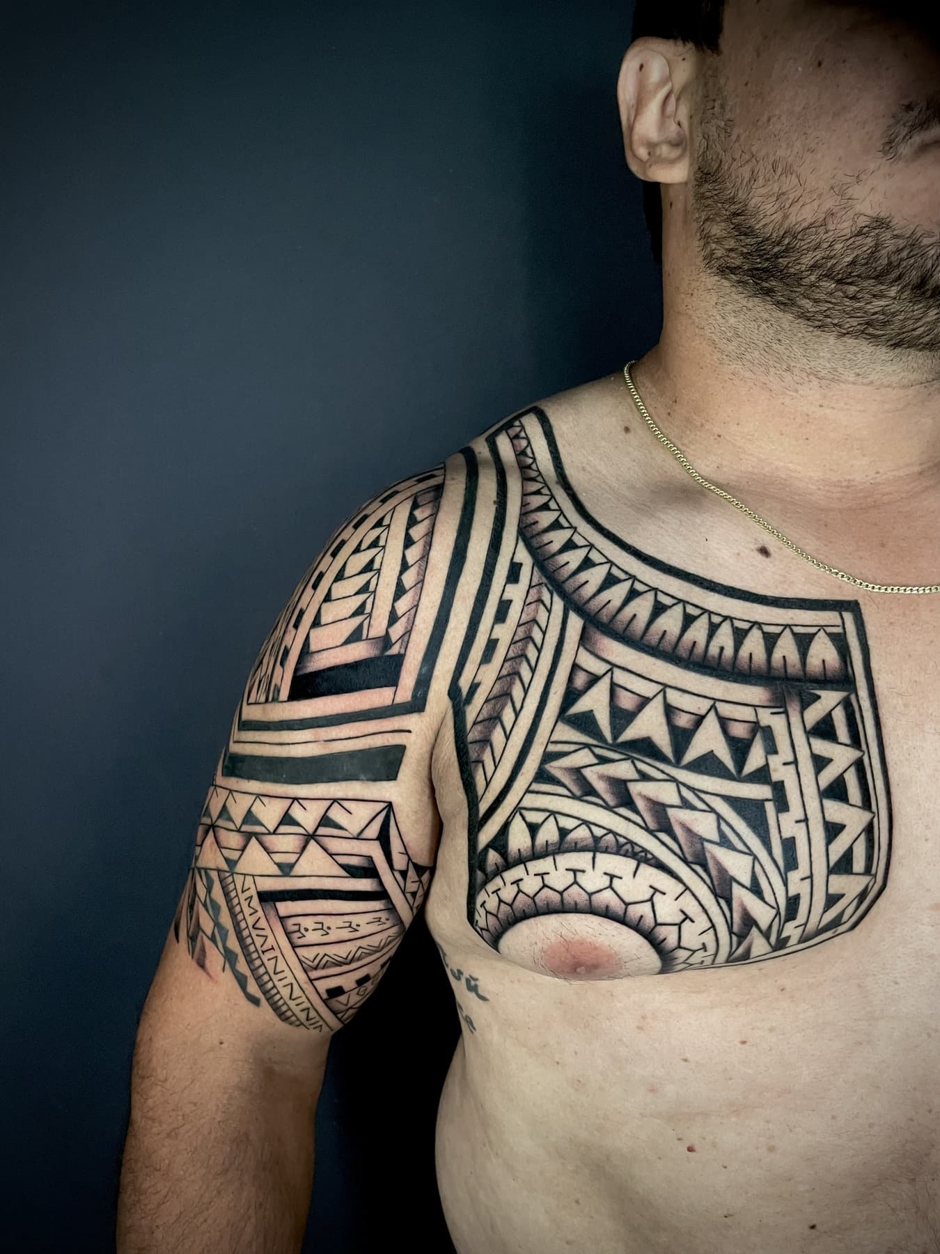 Peito e ombro em tribal polinésio, com faixas geométricas acompanhando a musculatura.